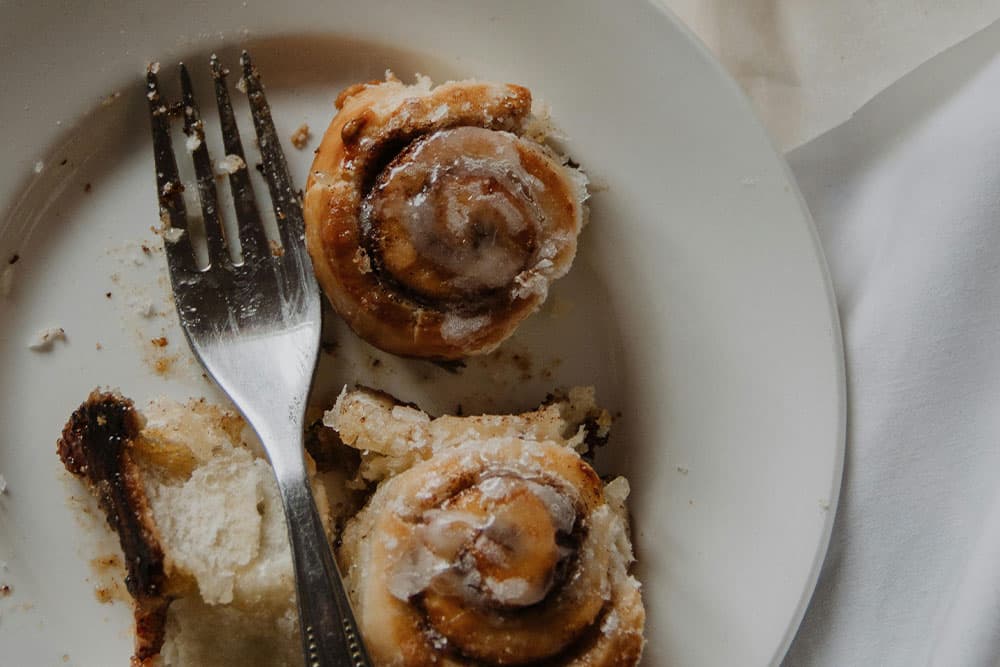 Two partially eaten cinnamon rolls on a plate with a fork.