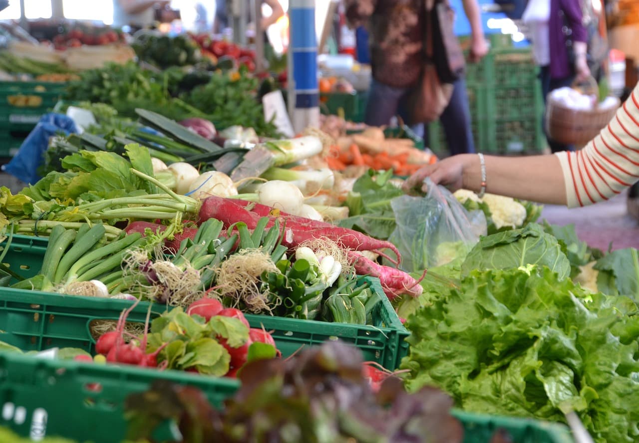 A colorful assortment of fresh vegetables displayed in baskets at a market, with a hand selecting produce. A colorful assortment of fresh vegetables displayed in baskets at a market, with a hand selecting produce.