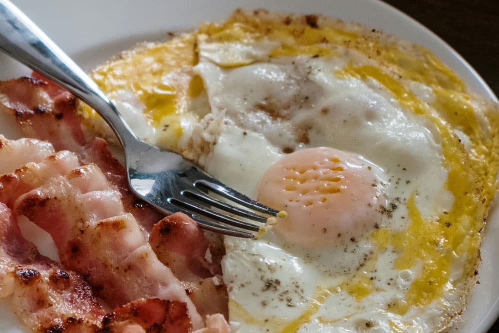 A plate of fried eggs and crispy bacon with a fork.