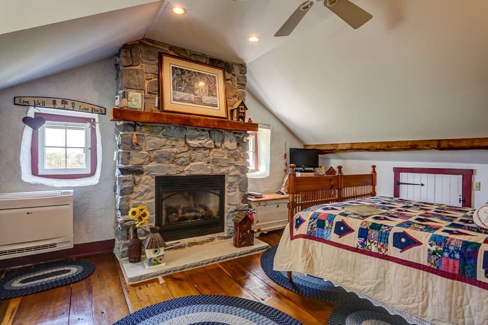 A cozy bedroom featuring a stone fireplace, quilted bedspread, and rustic decor.