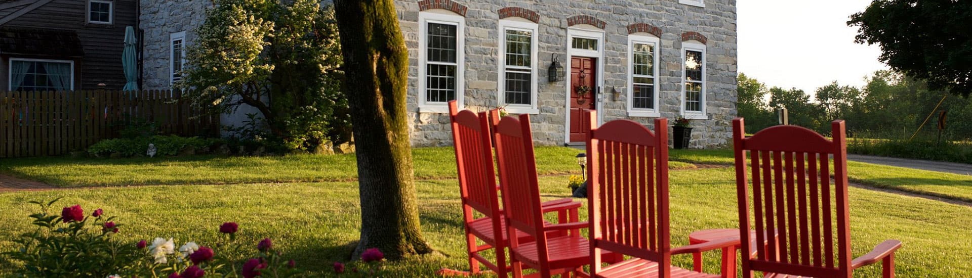 A cozy yard features several red rocking chairs in front of a charming stone house.