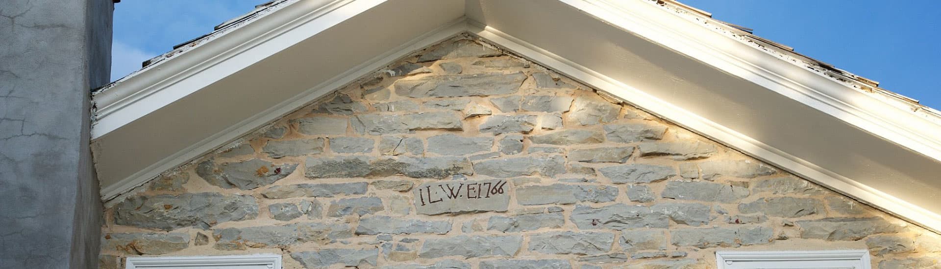 Close-up of a stone wall with the inscription "IL W E 1766" near the gabled roof.