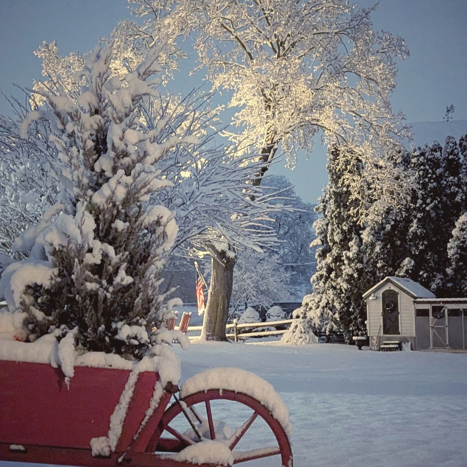 A snow-covered red wagon sits in a serene winter landscape illuminated by soft light. A snow-covered red wagon sits in a serene winter landscape illuminated by soft light.