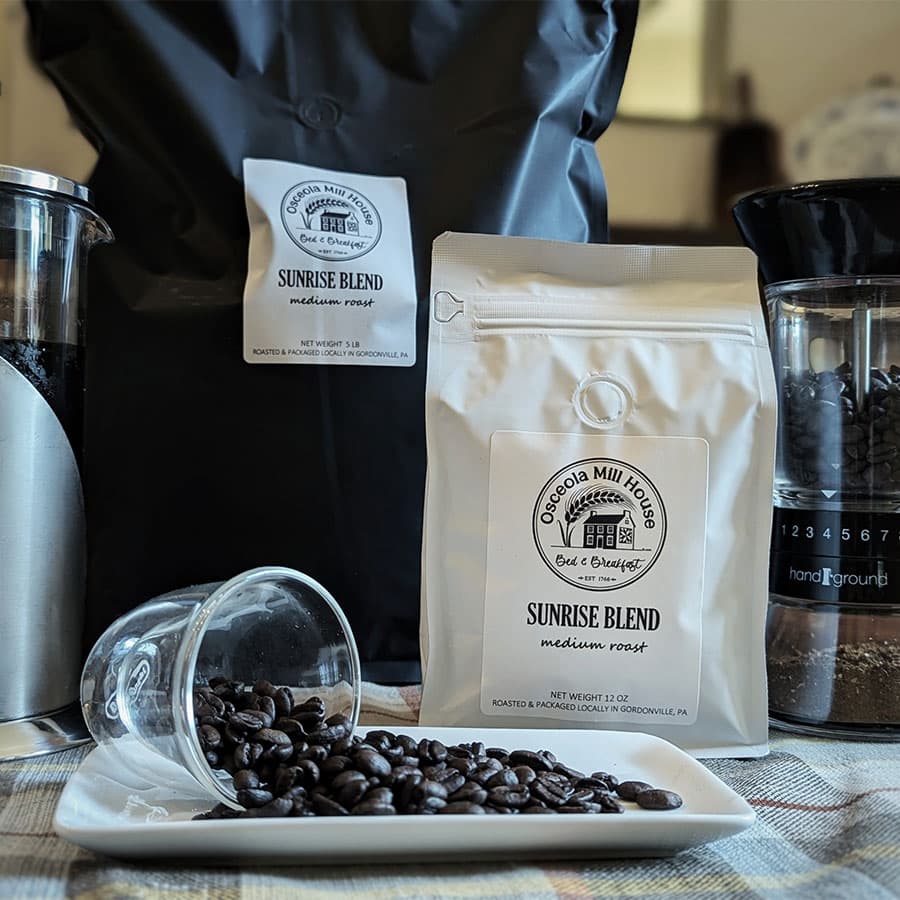 Two bags of "Sunrise Blend" medium roast coffee beside a glass of spilled coffee beans and a grinder.