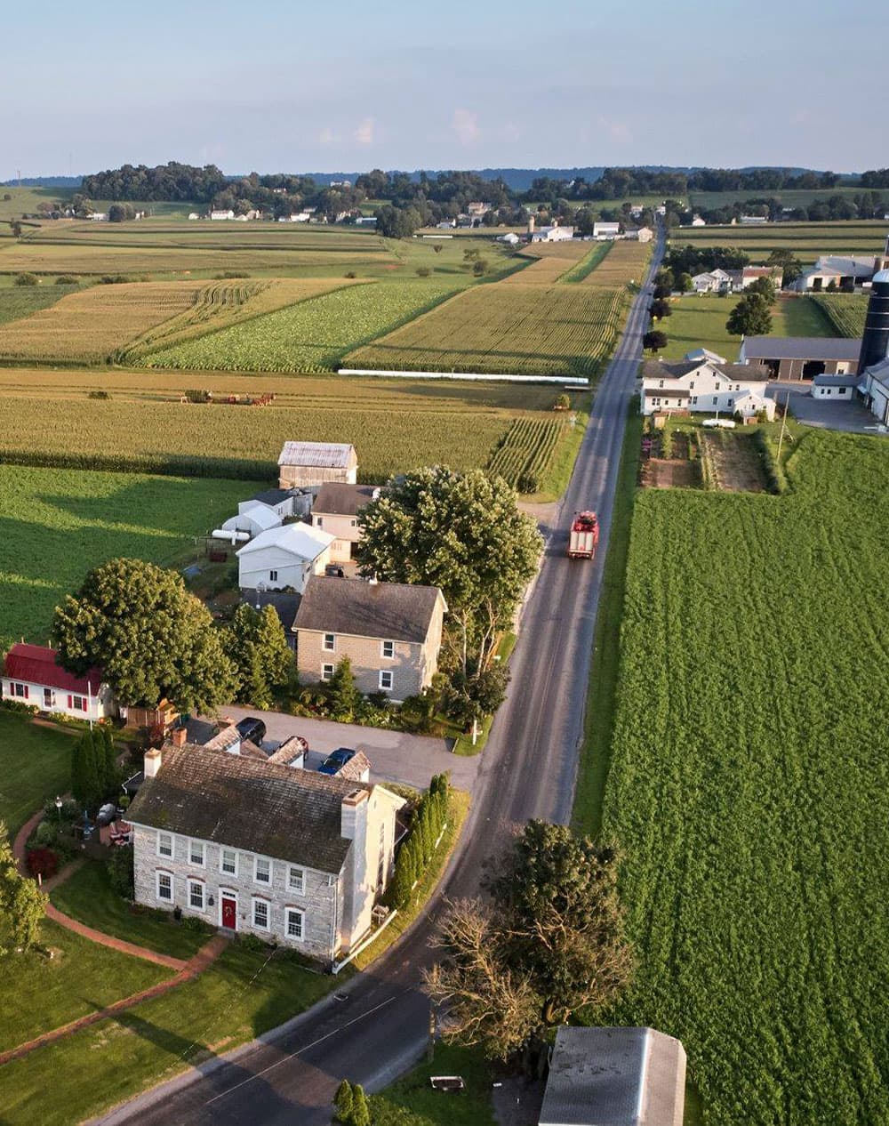 Aerial view of a rural landscape featuring fields, houses, and a winding road.