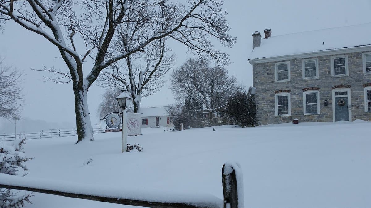 A snowy landscape featuring a historic stone house and bare trees under overcast skies.
