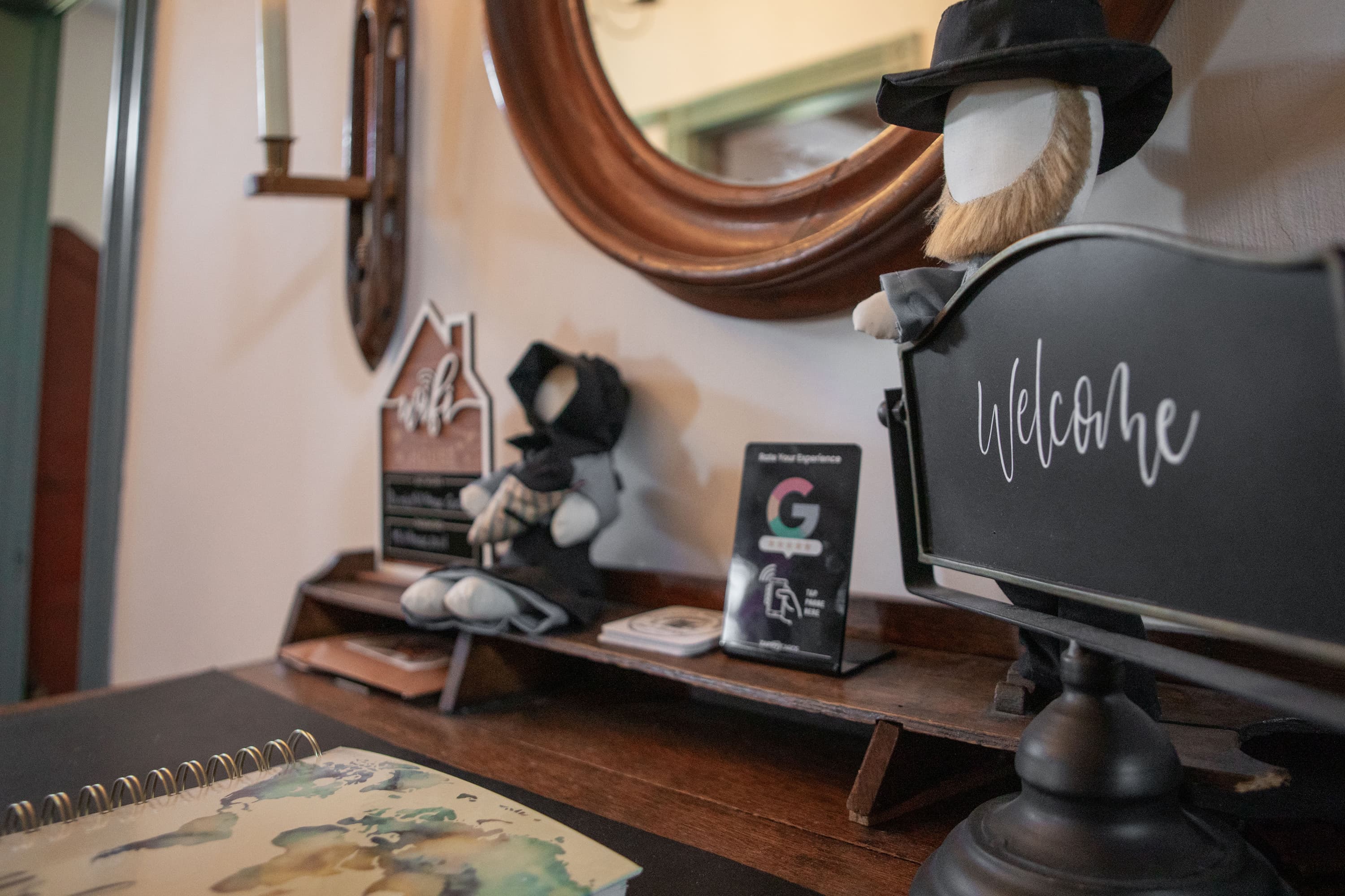 A rustic entryway with a decorative shelf, featuring a welcome sign, a small doll, and promotional materials. A rustic entryway with a decorative shelf, featuring a welcome sign, a small doll, and promotional materials.