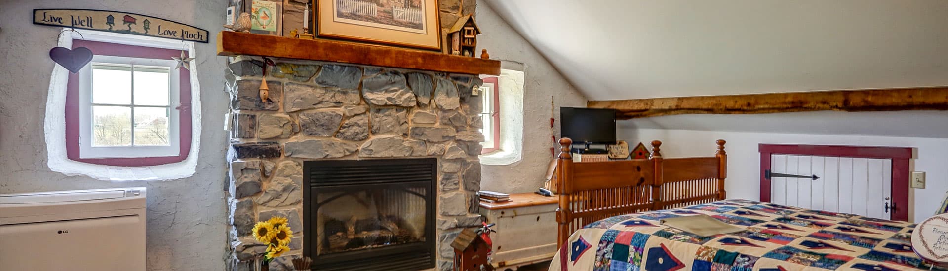 A cozy bedroom with a stone fireplace, colorful quilt, and rustic decor.